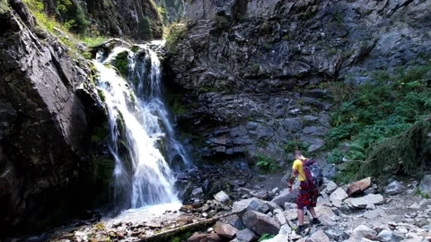 A guy with a backpack is standing near a waterfall Vídeos de archivo 160681533