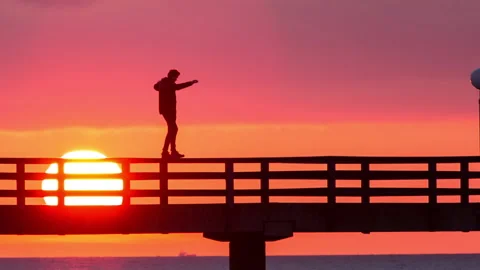 Guy balancing on a pier closer sunset silouette Stock Footage 153515630