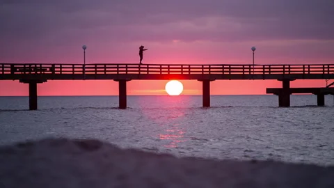Guy balancing on a pier extremwide beach foreground sunset silouette Stock Footage 153515641