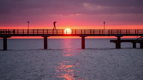 Guy balancing on a pier wide sunset silouette Stock-Footage 153515660