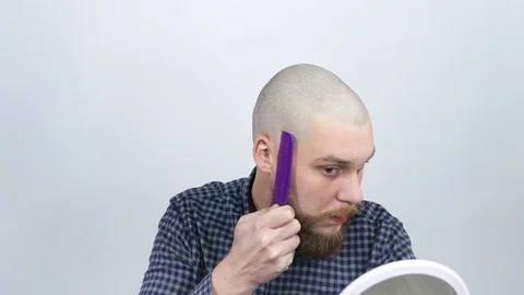 The guy with the bald head looks in the mirror and combing his beard Stock Footage 122005459