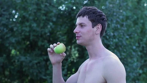 A guy with a bare torso eating an apple in the open air Stock Footage 78938517