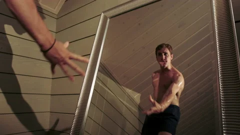 A guy with a bare torso stands near a mirror and poses. Stock Footage 197481151