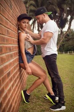 Guy in a baseball cap and black pants poses with a beautiful girl in blue sh Stock Photos