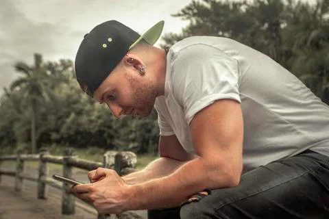 A guy in a baseball cap sits on the railing and writes sms Stock Photos