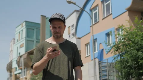 A guy in a baseball cap walks through the city in the summer with a phone Vidéo 313360014