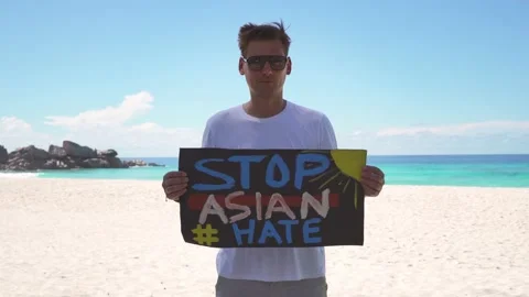 A guy on the beach is standing with a poster that says "Stop Asian Hate" Video stock 154668843