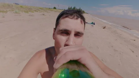A guy on the beach takes a plastic bottle and drinks water from it. Thirst. Vídeos de archivo 339931641