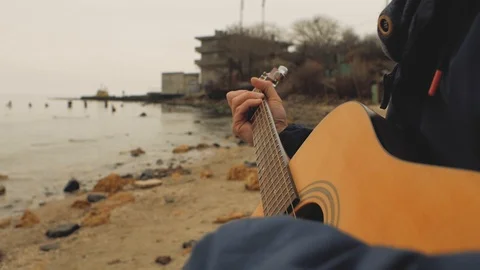 A guy with a beard and a hat playing a guitar near the sea Stock Footage 103141036