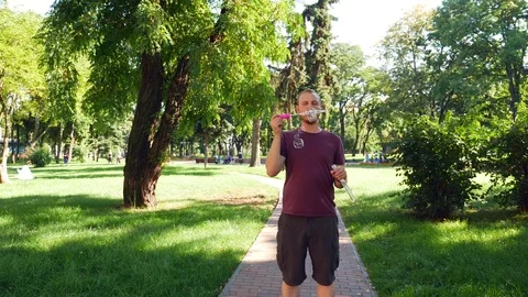 Guy with a beard blows soap bubbles. In the park a sunny day Stock Footage 114052418