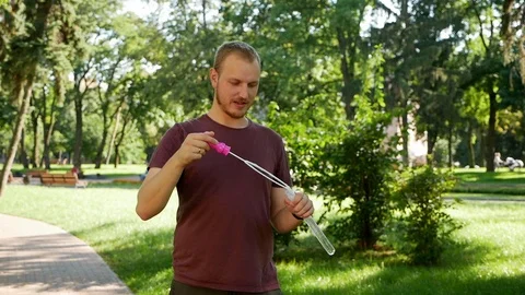Guy with a beard blows soap bubbles. In the park a sunny day Stock Footage 114109913