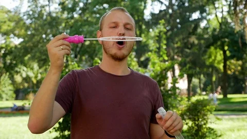 Guy with a beard blows soap bubbles. In the park a sunny day Stock Footage 114109944