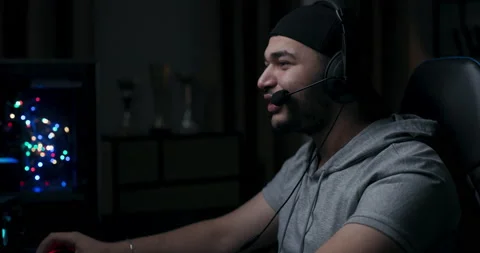Guy with beard in gray t-shirt and black cap is playing online game. Player Stock Footage 214135929