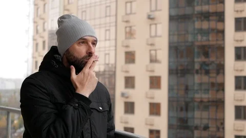 The guy with the beard is standing on the balcony smoking a cigarette Stock Footage 99572904