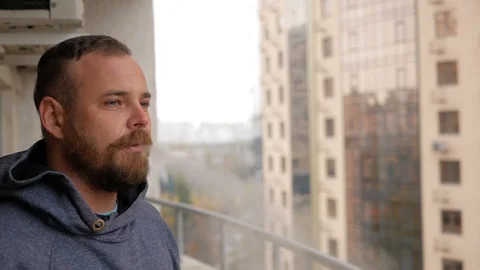 The guy with the beard is standing on the balcony, smoking and pointing to th Stock Footage 99572924
