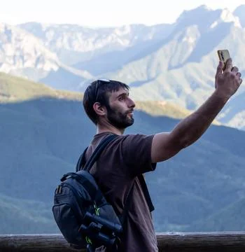 Guy with beard wearing backpack with binoculars taking a selfie in the mounta Stock Photos