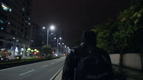 A guy in black clothes with a backpack is walking along the street of night city Stock Footage 110703120