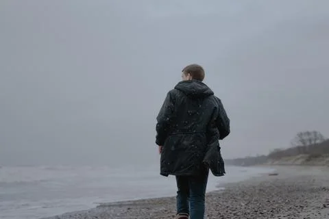 A guy in a black jacket run along the sandy cloudy sea Stock Photos