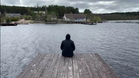 A guy in a black jacket is sad and looks into the distance next to the sea light Stock-Footage 205833070