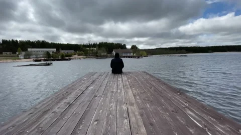 A guy in a black jacket is sad and looks into the distance next to the sea light Stock Footage 205833076