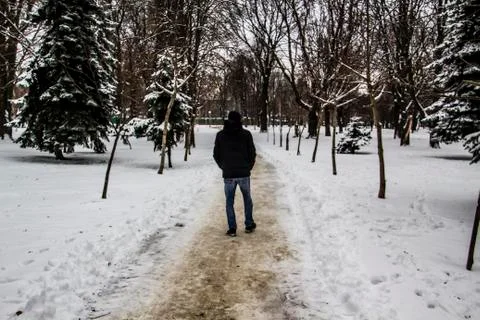 A guy in a black jacket is walking along the road. Silhouette of a man. Winte Stock Photos