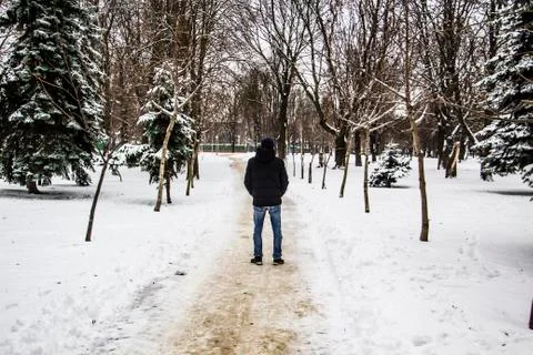 A guy in a black jacket is walking along the road. Silhouette of a man. Winte Stock Photos