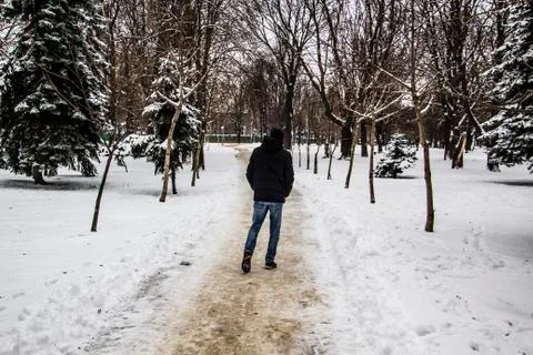 A guy in a black jacket is walking along the road. Silhouette of a man. Winte Stock Photos