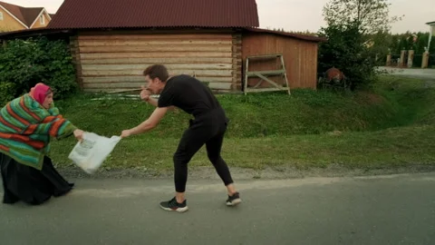 A guy in a black suit wants to help an old woman carry heavy bags of food. Stock Footage 197480700