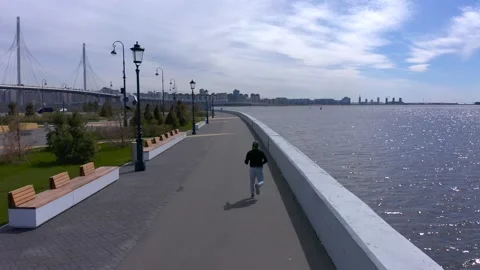 A guy in a black sweater and gray pants is running along the promenade Stock Footage 131416922