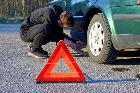 The guy in the black tracksuit put the jack under the car. Stock Photos