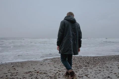 A guy in a black warm jacket walks along the seashore, stands sepina Stock Photos