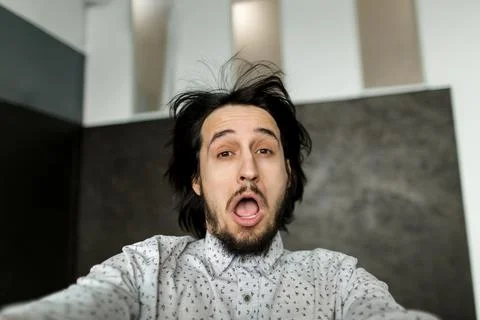 Guy blows with wind he looks at camera, guy has a beard mustache and long hair. Stock Photos
