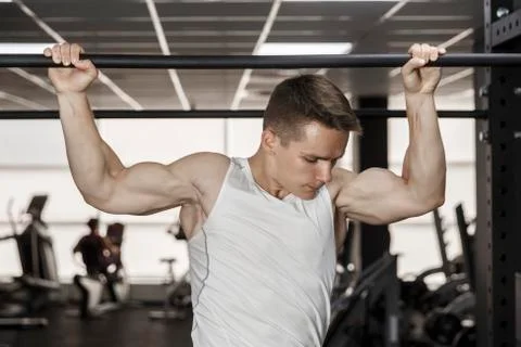 Guy bodybuilder execute exercise pulling up on horizontal bar in gym, horizon Stock Photos