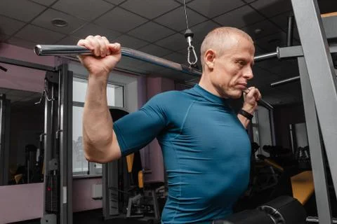 Guy bodybuilder, perform exercise with exercise machine on broadest muscle of Stock Photos