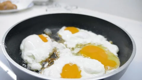 The guy breaks chicken eggs and fries them in a griddle, on an induction cooker. Stock Footage 107153716