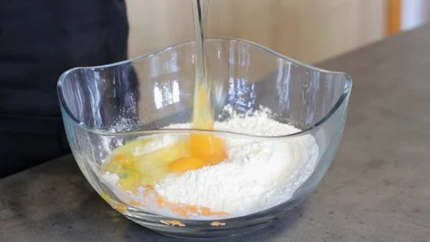 The guy breaks the egg in a glass plate, which is flour and other yolks of eggs. Stock Footage 112939459