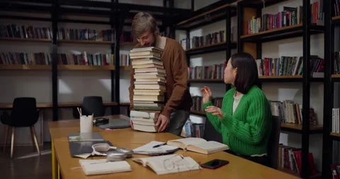 A guy brings a large stack of books and sits next to his girlfriend while Stock Footage 313356942