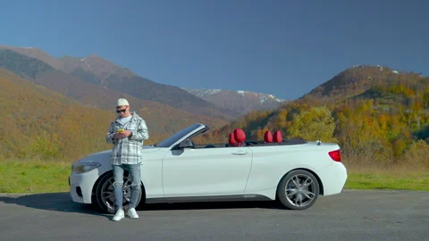 Guy is browsing in smartphone standing near convertible car on mountain road. Stock Footage 260958478