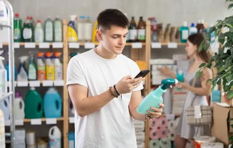 Guy buyer scans qr code on tile cleaner spay label, girl shopping in background Foto stock
