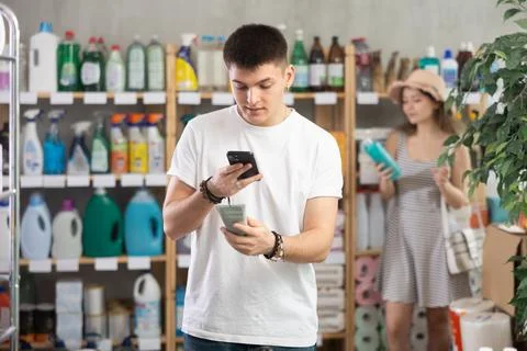 Guy buyer scans qr code on sunblock cream label, woman shopping in background Foto stock
