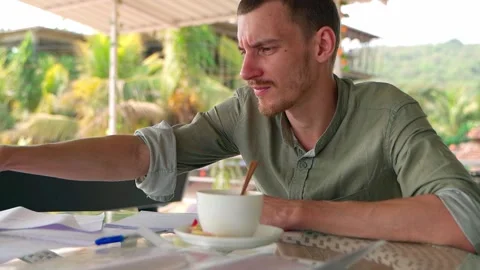 The guy is in a cafe and writing in his notebook, taking his phone in his hand. Video stock 231337042