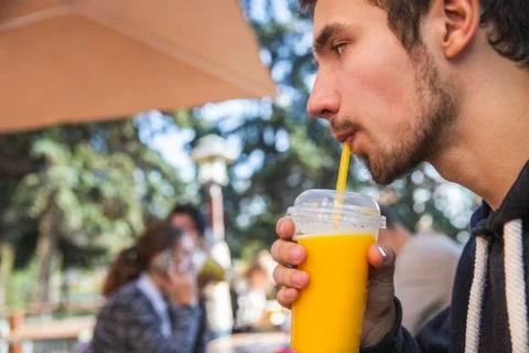 A guy is calmly drinking his fruit juice while sitting at the fastfood terrac Stock Photos