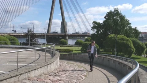 Guy with camera on tripod walks along road on sunny day Stock Footage 139797742