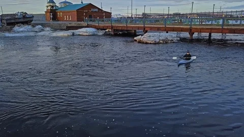 Guy in canoe sails against metal bridge between snowy banks 스톡 동영상 123864591