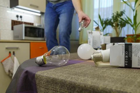 Guy in casual wear changes light bulbs in kitchen from incandescent bulbs to LED 스톡 사진