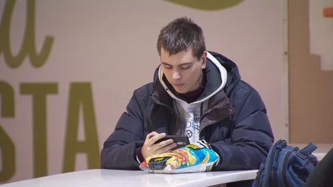 Guy with chips and a mobile phone sits on a food court. fast food restaurant Stock Footage 129327723