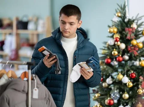 Guy chooses a set of socks against the background of a Christmas tree Stock Photos