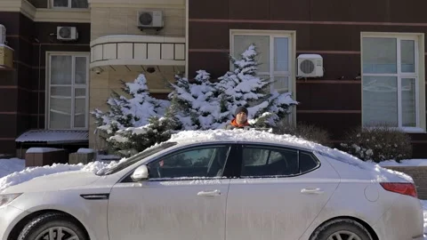 A guy cleans fresh snow from his car with a brush on a bright sunny day.Cleaning Stock Footage 160987395