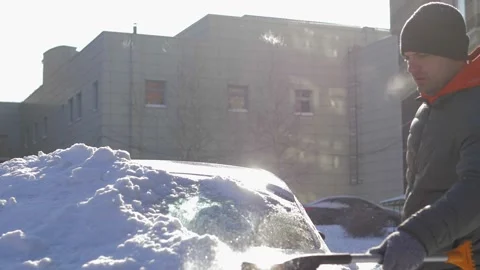 A guy cleans fresh snow from his car with a brush after a blizzard on a bright Stock Footage 160987952