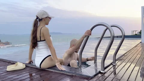 Guy climbs down ladder pool sunset. Sea views backdrop. Stock Footage 329410083